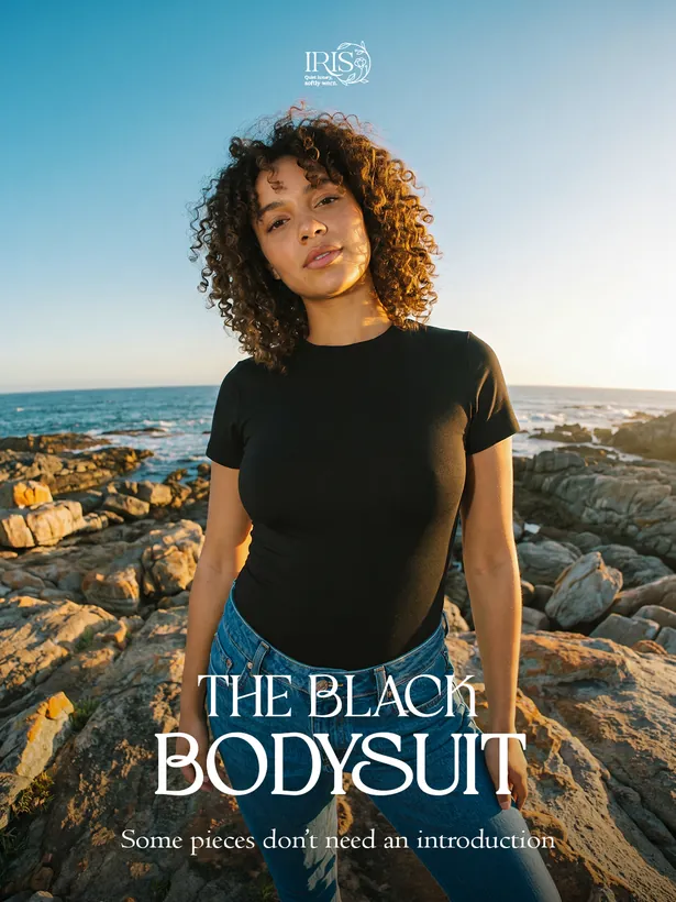 IRIS campaign image: a model in a black bodysuit on a rocky shoreline at golden hour, headline The Black Bodysuit.