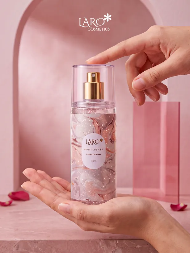 Product photograph: the marbled Night Shimmer body splash held in two hands against a pink arch, rose petals on the ledge.